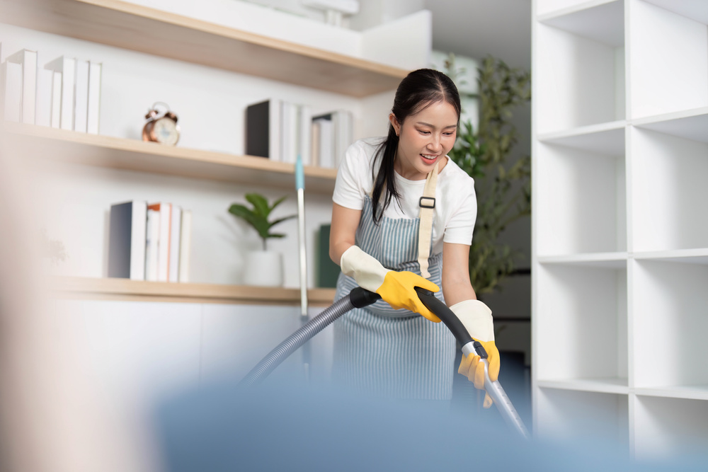 Home Cleaning. Joyful woman vacuuming while listening to music in a modern living room